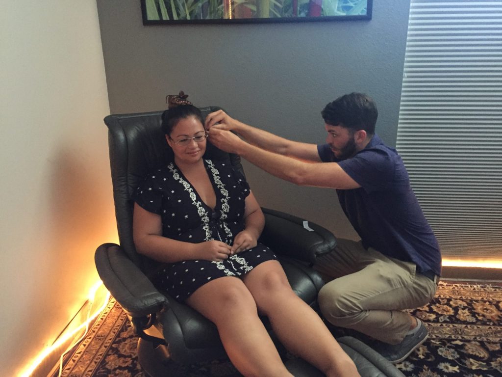 woman seated in chair receiving auricular acupuncture treatment